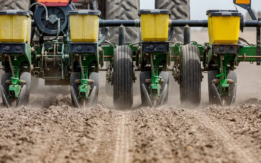 Closeup of tractor and planter in farm field planting corn or soybeans seed in dry, dusty soil during spring season